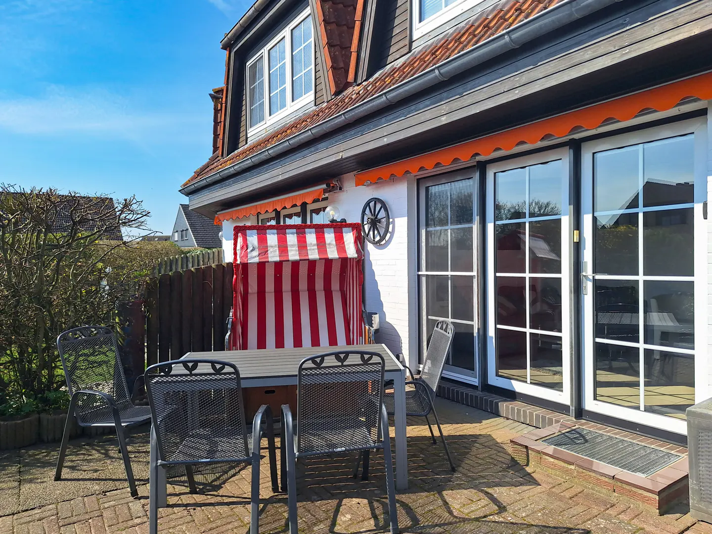 Outdoor patio with metal table and chairs, red and white striped beach chair, and white house with orange awnings.
