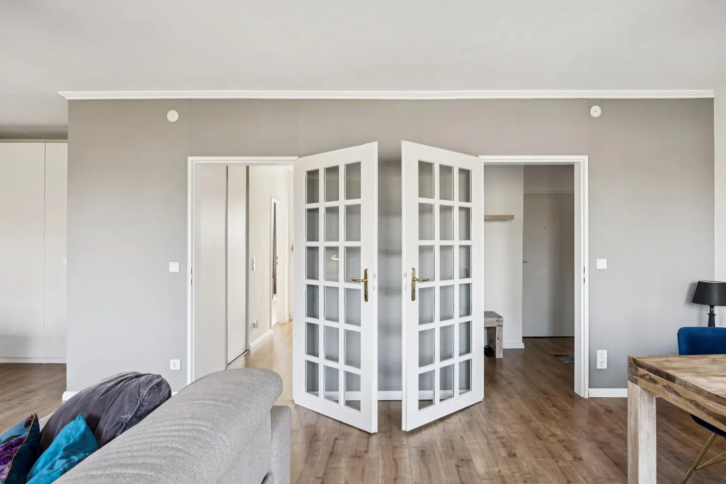 Interior view of a gray room with open white French doors, wood floors, and a gray sofa in the foreground.