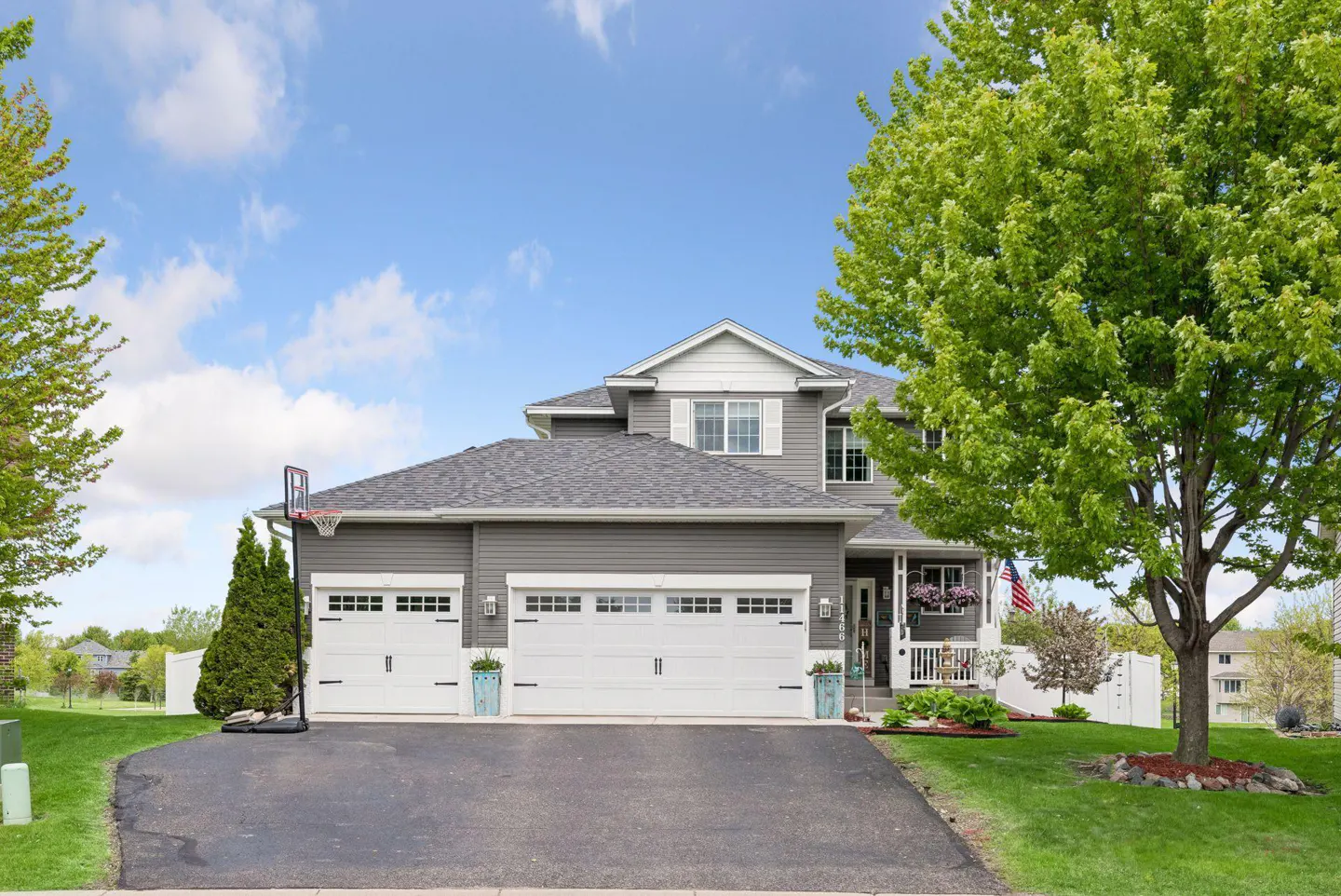 Two-story gray house with a three-car garage, white trim, and a basketball hoop on the driveway.