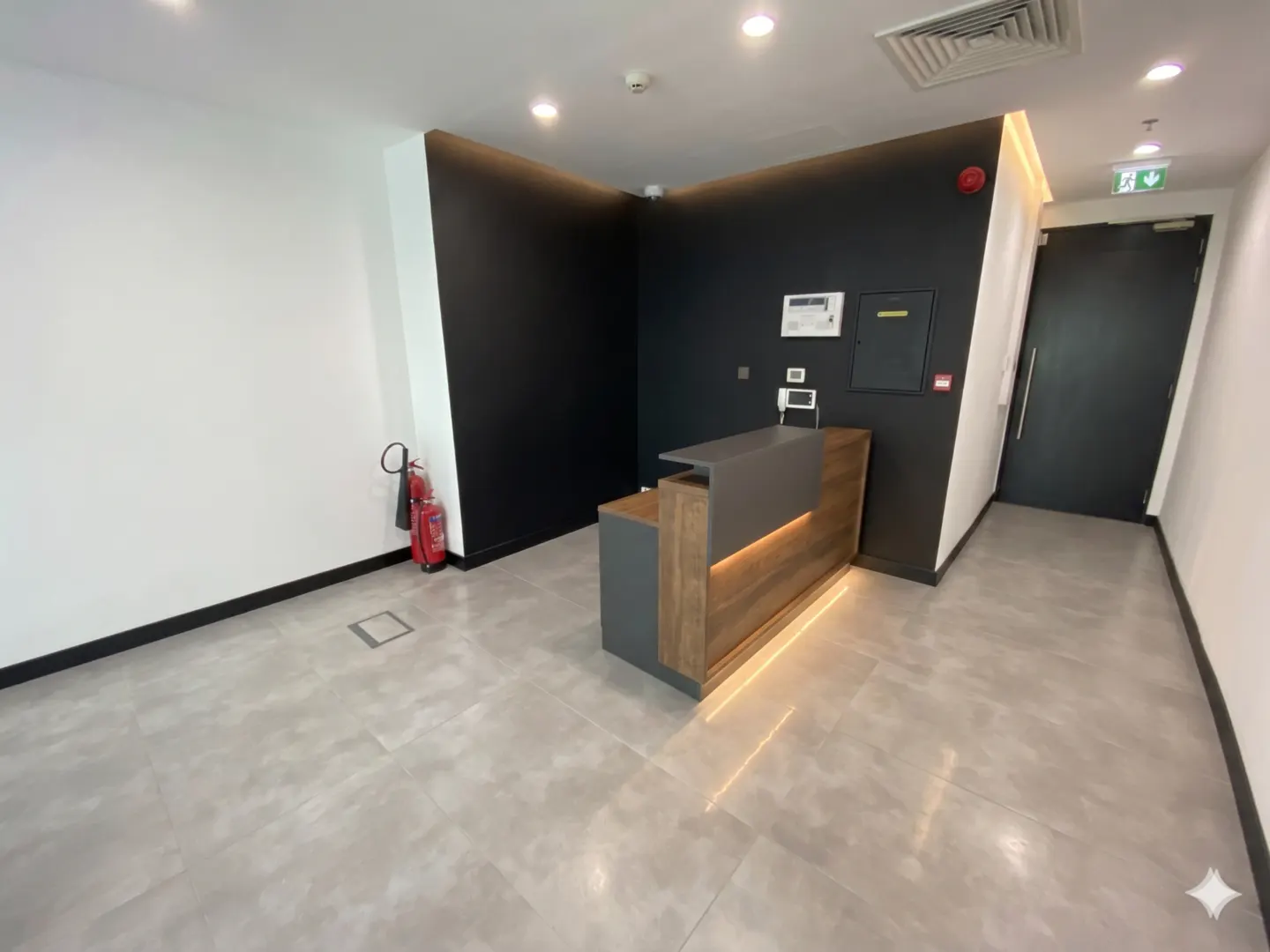Office lobby with a gray and wood reception desk, black accent wall, and gray tile floor. A red fire extinguisher is visible.
