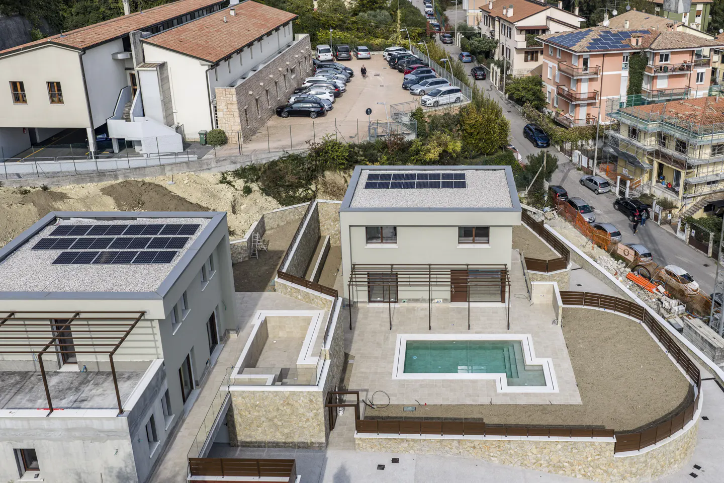 Aerial view of two modern, light gray homes with solar panels and pools in a residential area.