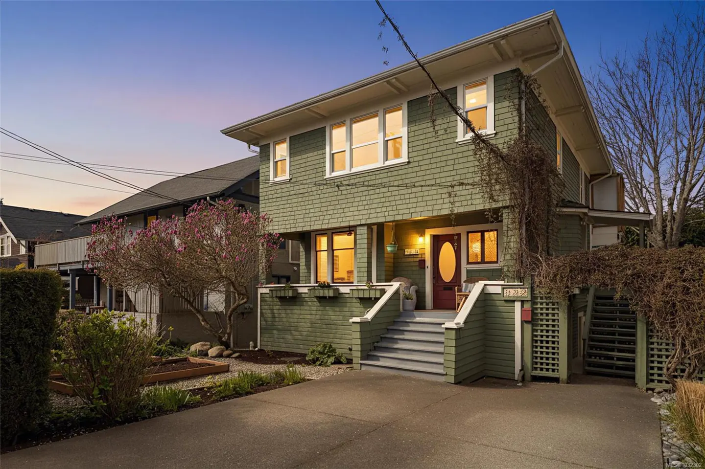 Two-story green house with a red door and gray stairs. A tree with pink flowers is on the left.