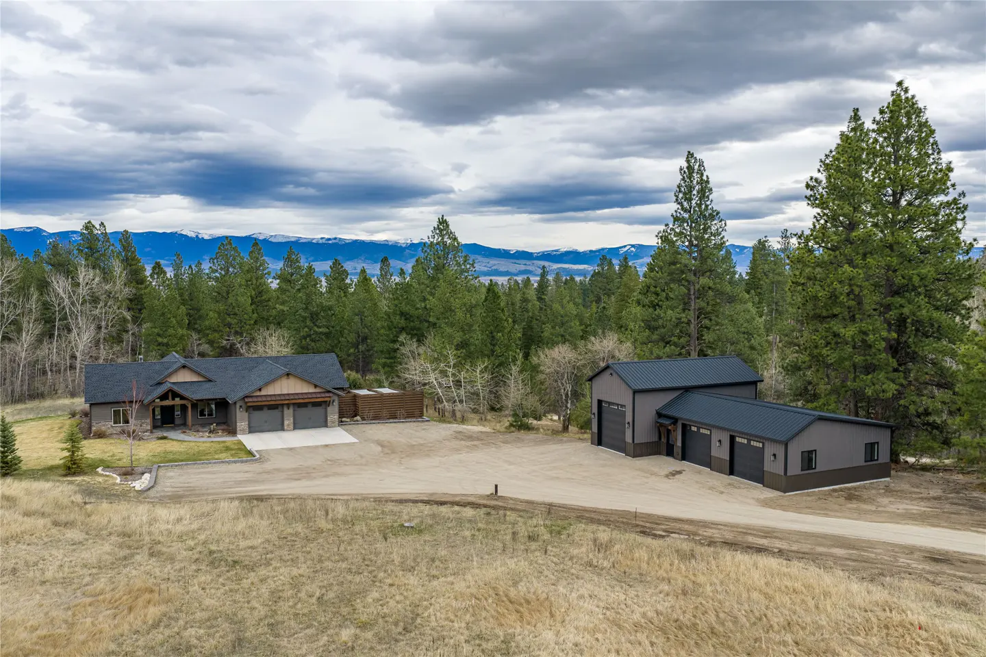 A landscape view of a house and garage surrounded by trees and mountains.