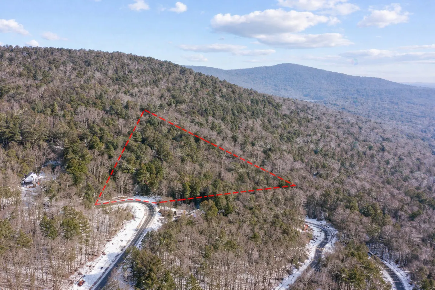 Aerial view of wooded land outlined in red, with a winding road and mountains in the background.