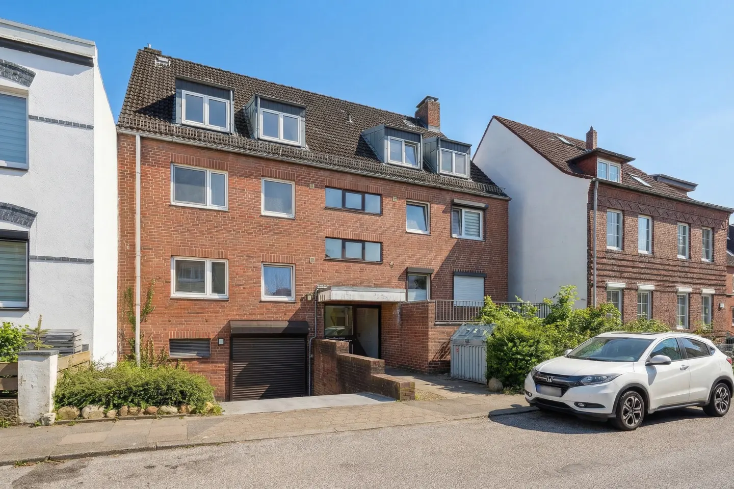 Three-story brick apartment building with a garage and a white car parked in front.