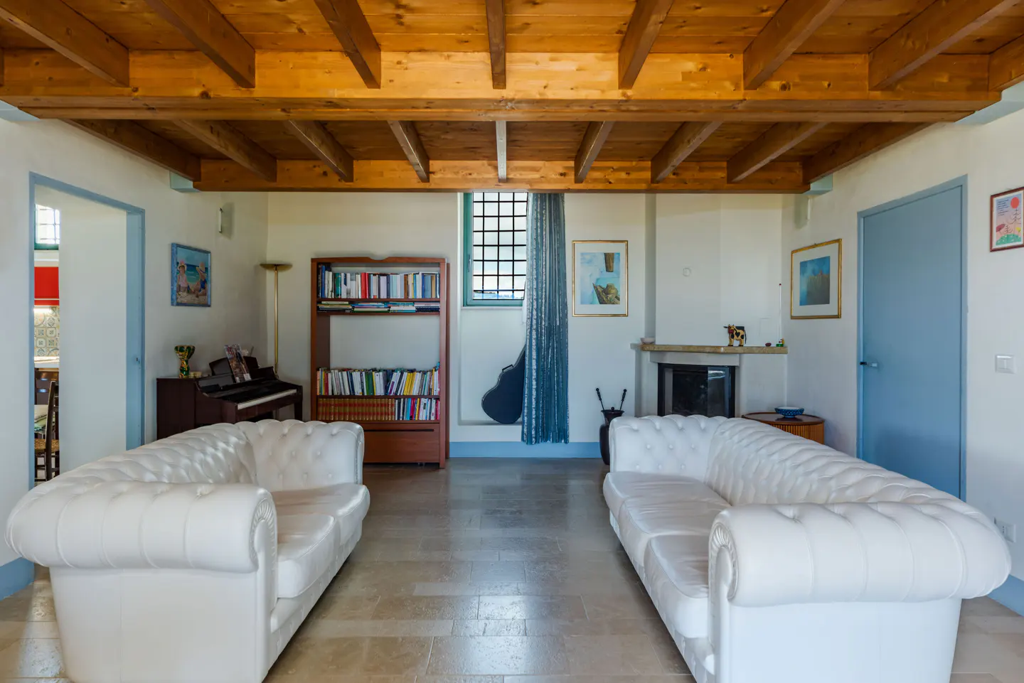 Living room with two white sofas, a wooden ceiling, a piano, and a bookshelf.
