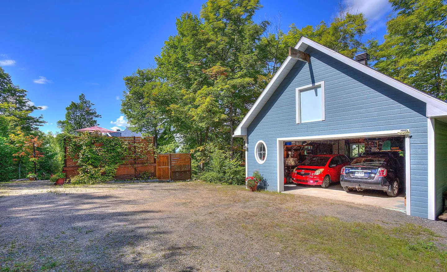 A blue garage with two cars inside, a red Toyota and a dark blue Nissan, on a sunny day.