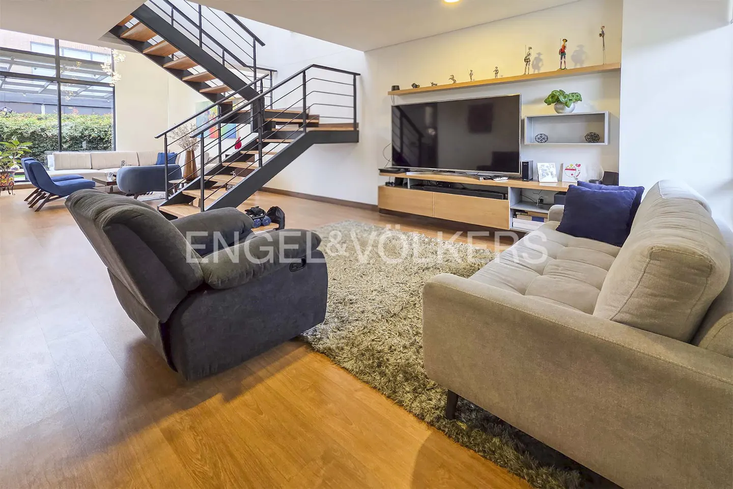 Living room with a gray recliner, a light gray sofa with blue pillows, and a black metal staircase with wooden steps.