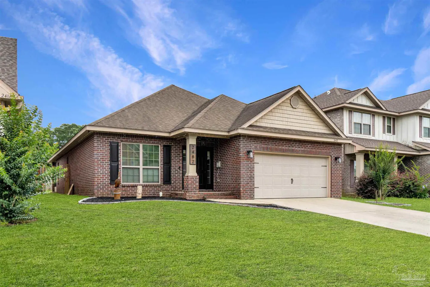 A single-story brick house with a tan garage door and a green lawn under a blue sky.