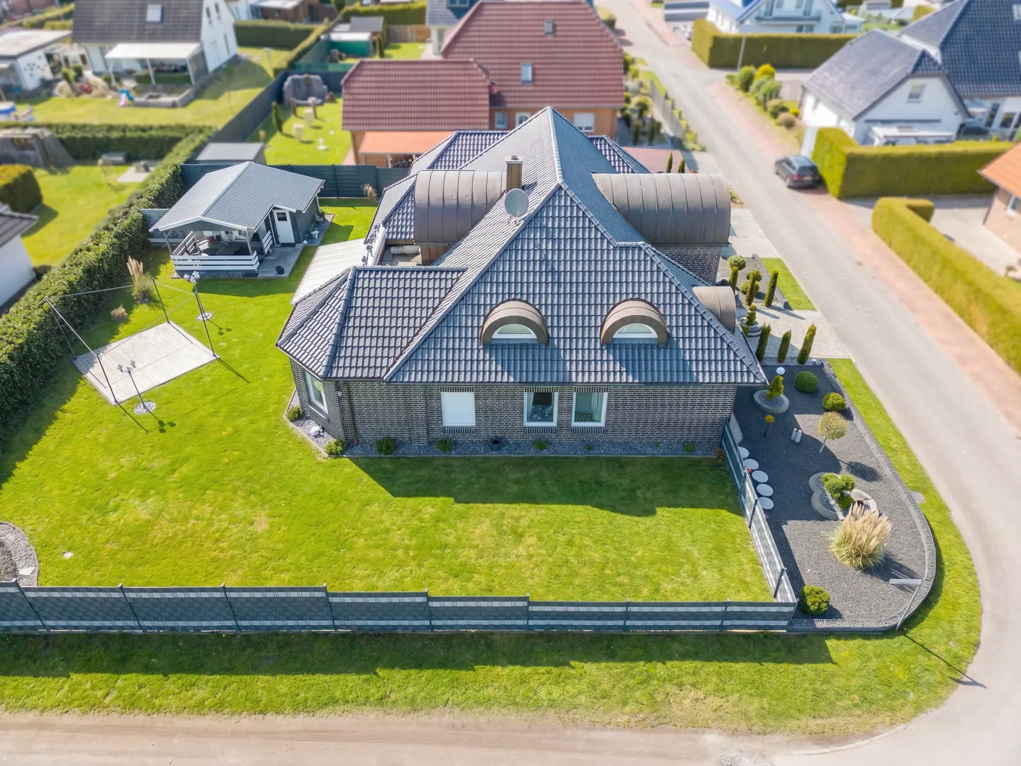 Aerial view of a brick house with a gray tiled roof, green lawn, and a gray fence.