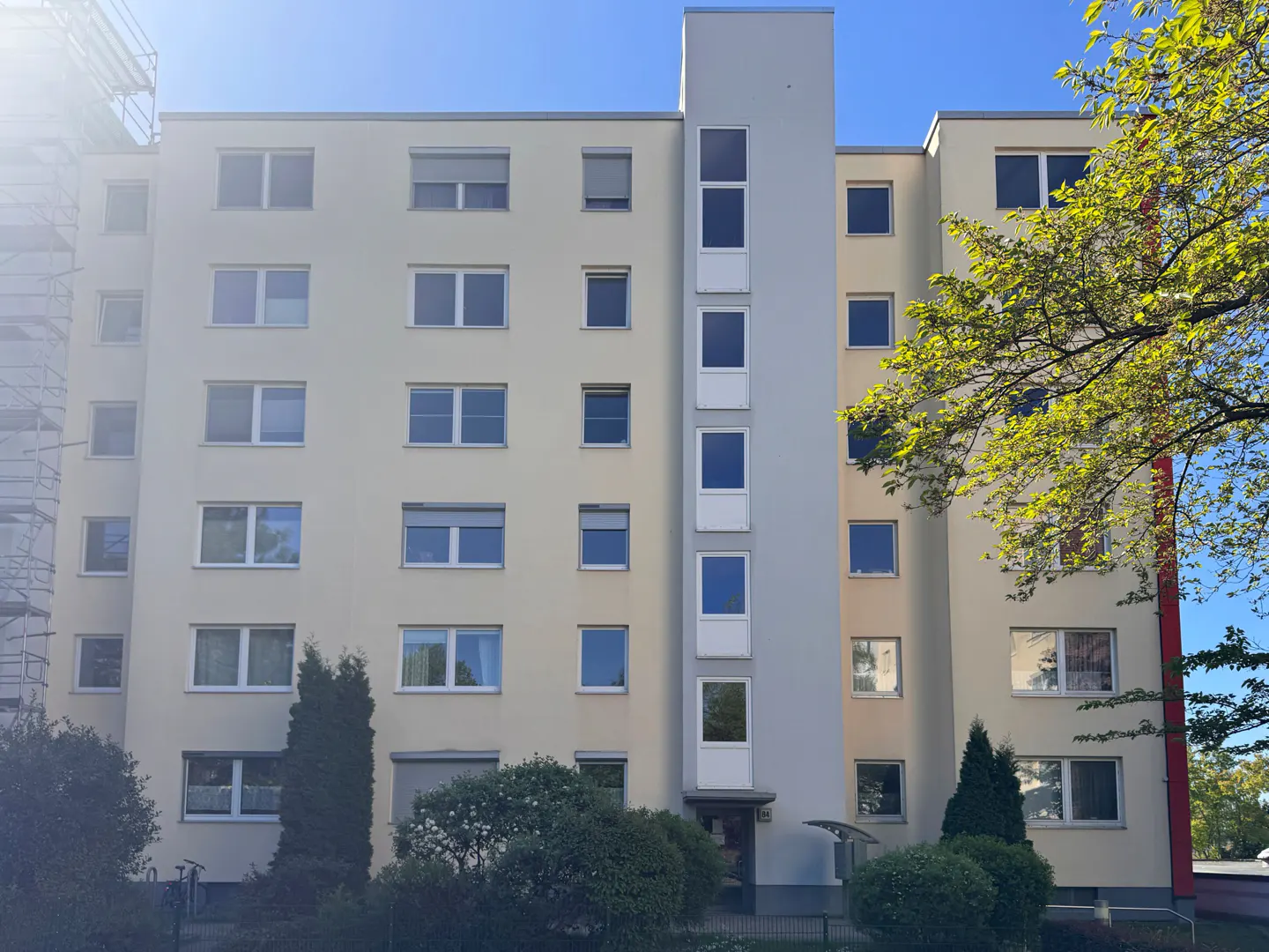 Exterior view of a multi-story apartment building with beige walls, a gray central tower, and many windows under a clear blue sky.