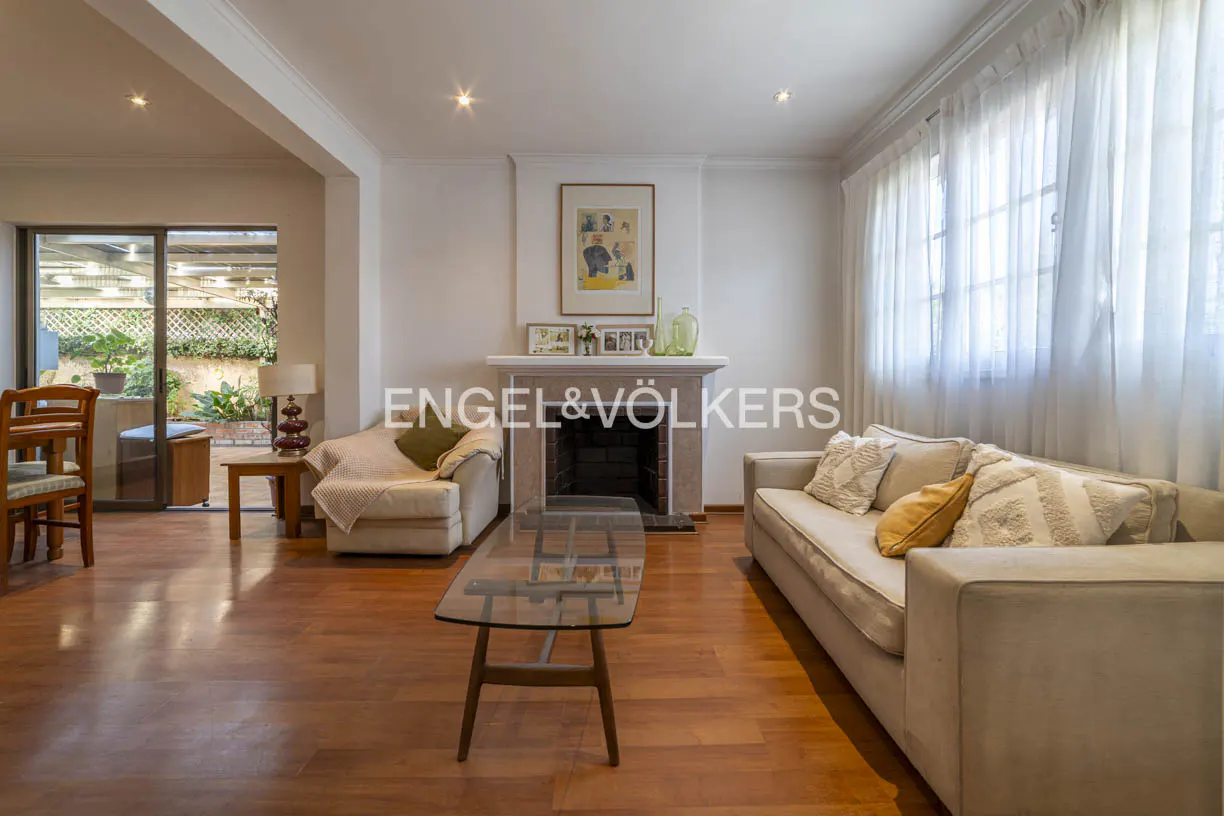Living room with hardwood floors, fireplace, and beige sofas. Sheer white curtains cover the windows. A glass coffee table sits in the center.