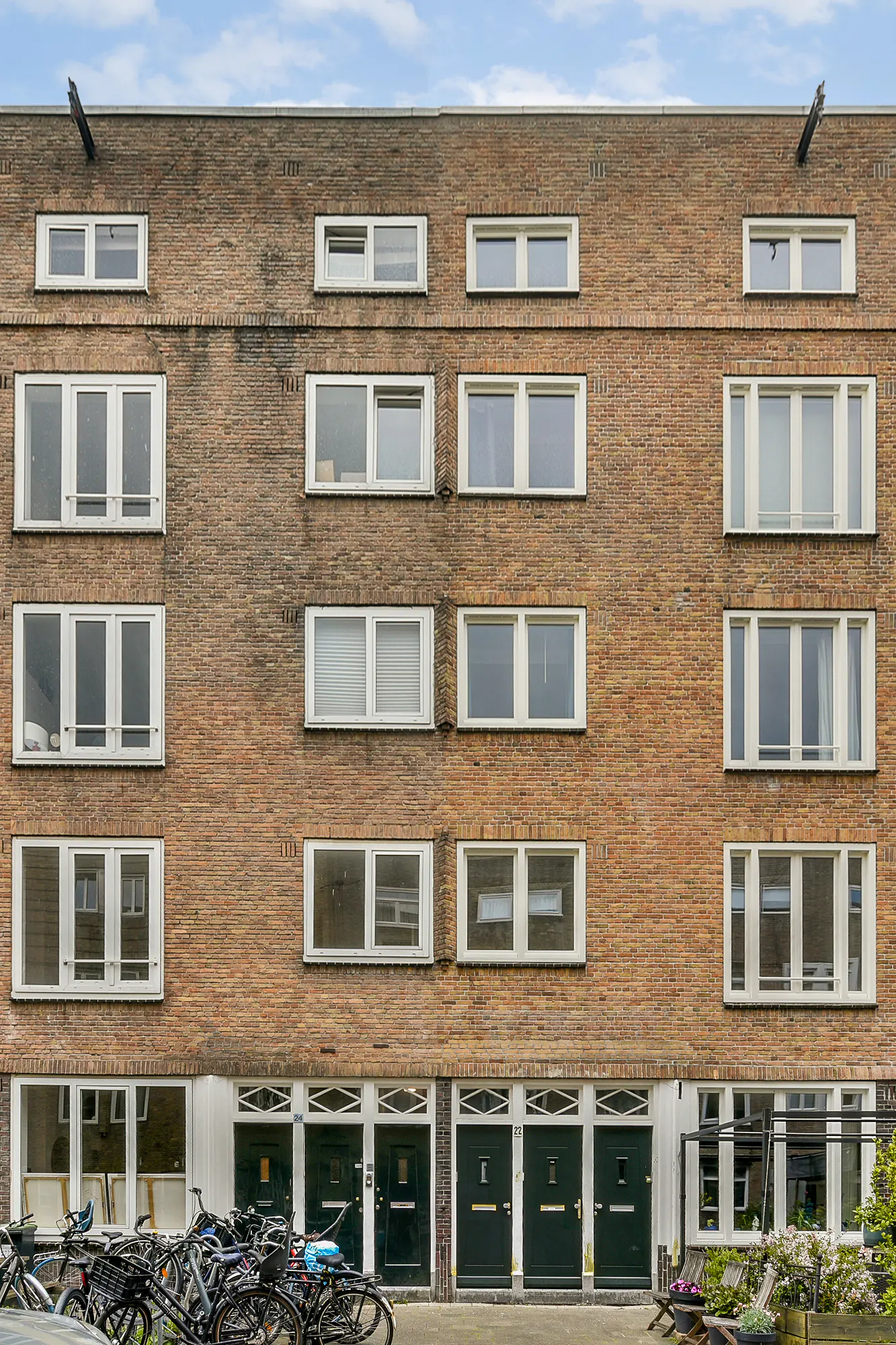 Exterior of a brick apartment building with rows of windows and dark green doors. Bicycles are parked in front.