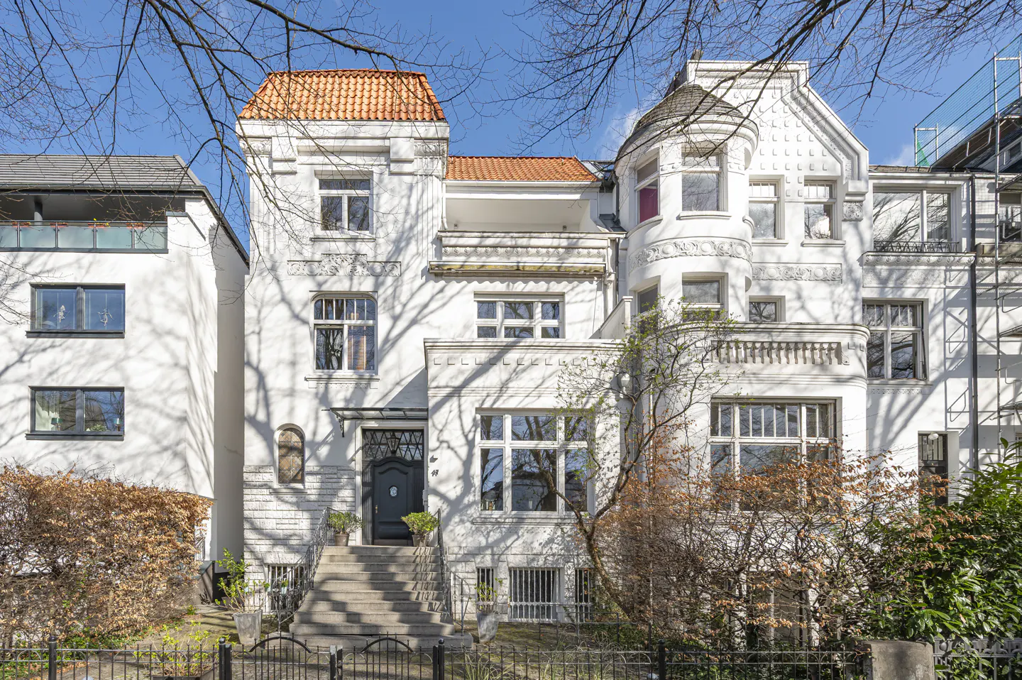 Exterior view of a three-story white house with a red-tiled roof and a black front door.