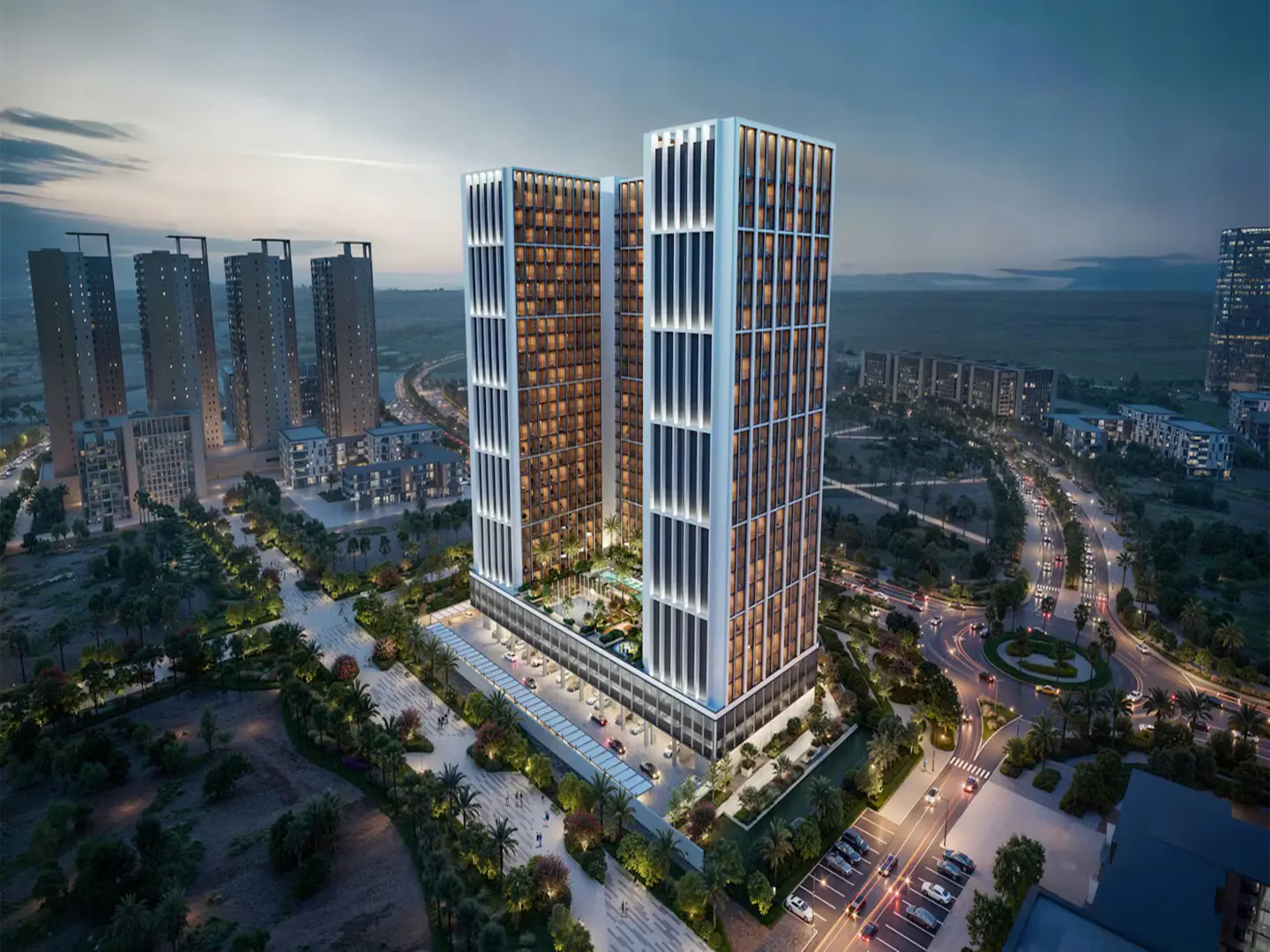 Aerial view of two modern, tall apartment buildings with white frames, surrounded by city streets, trees, and other buildings at dusk.