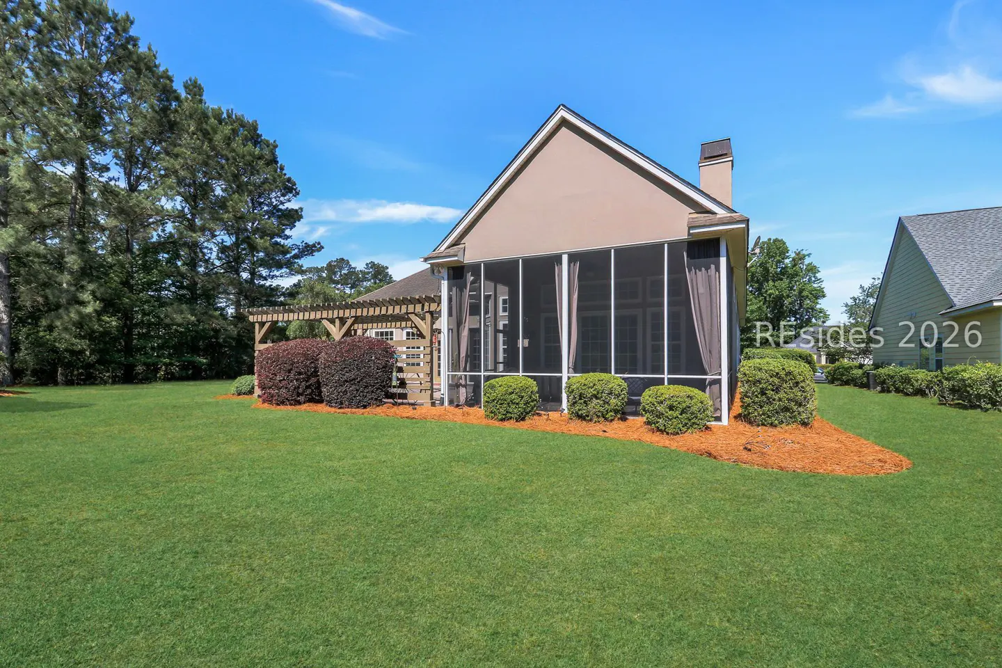 Exterior view of a house with a screened porch, pergola, green lawn, and blue sky.