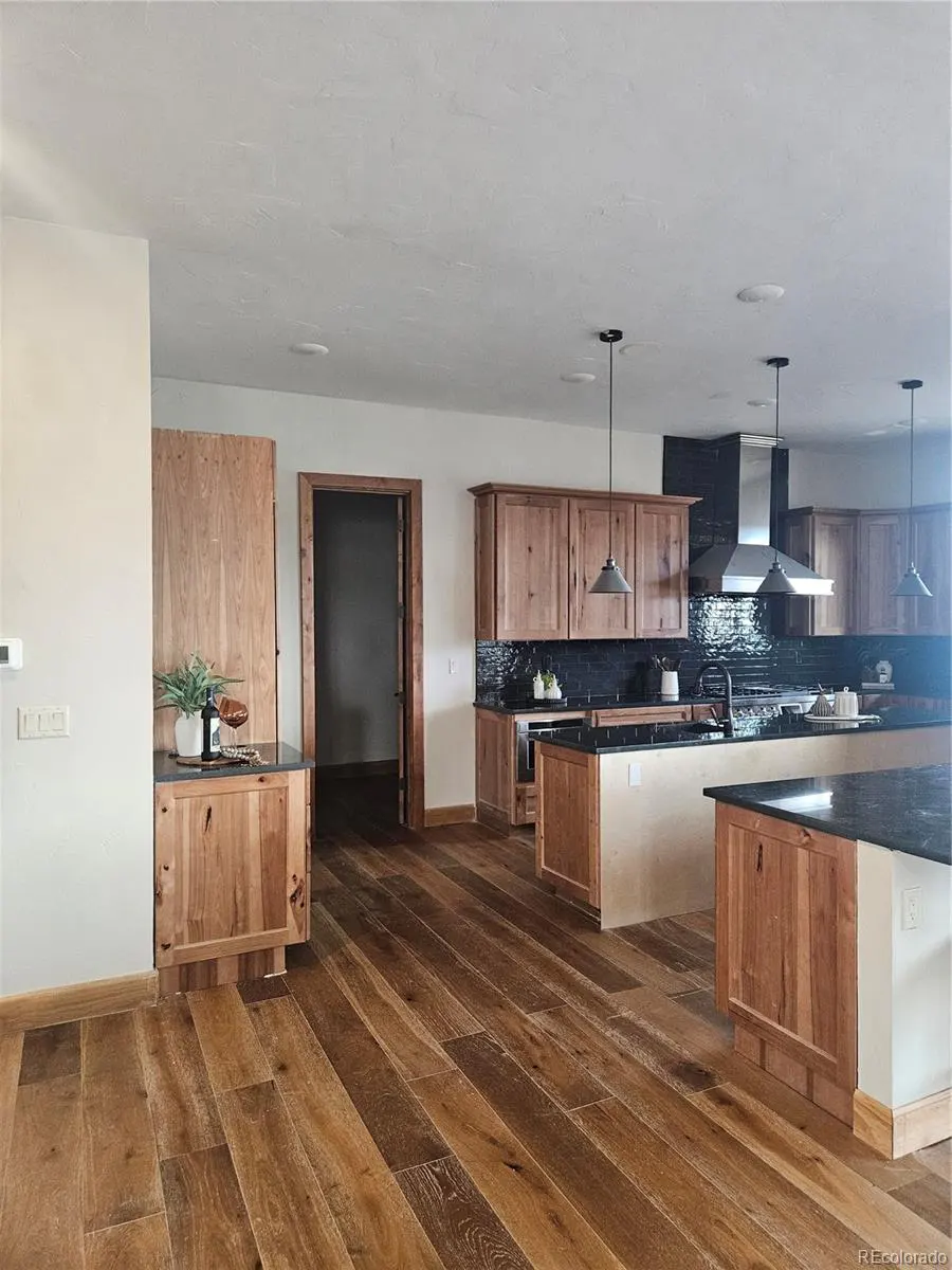A bright kitchen with wood floors, cabinets, and black countertops. A stainless steel range hood is centered on the back wall.