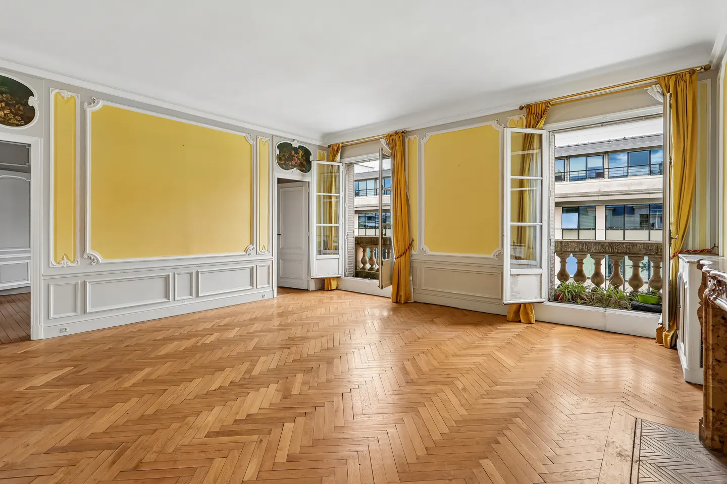 Empty room with herringbone wood floors, yellow paneled walls, and French doors opening to a balcony with city views.