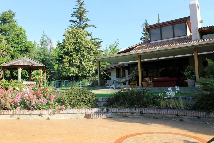 Backyard view of a house with a gazebo, flowers, and a hammock on the porch.