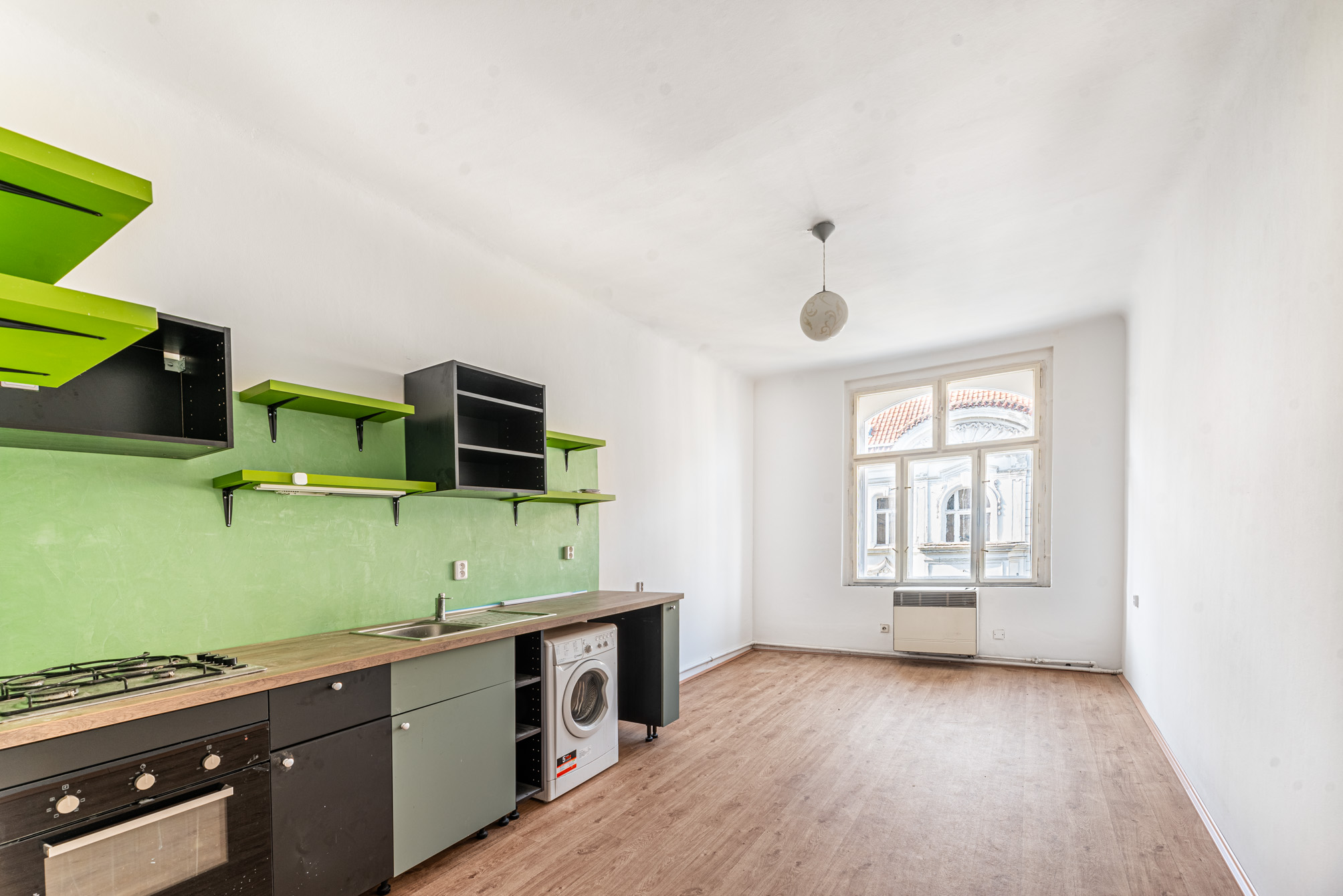Modern kitchen with green backsplash, black cabinets, built-in oven, washing machine, and a large window in a white room. [AI-generated text]