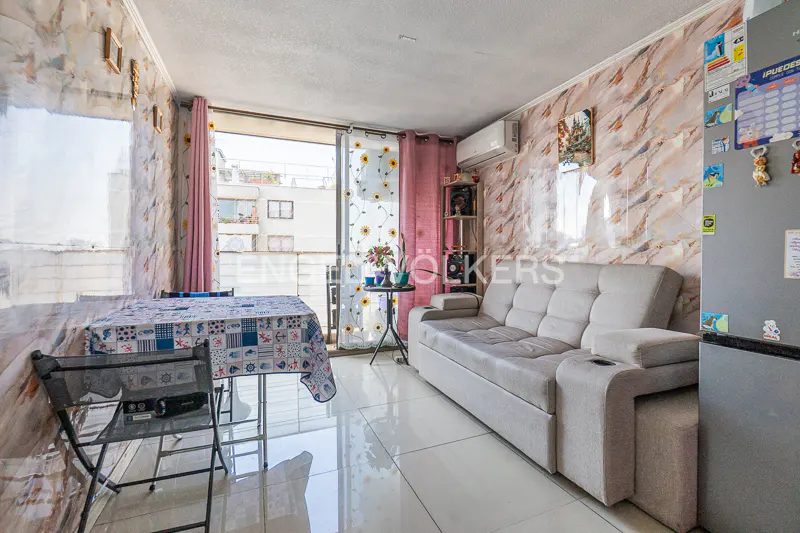 Living room with a gray sofa, table with a patterned tablecloth, and a view of a building through a sliding glass door.