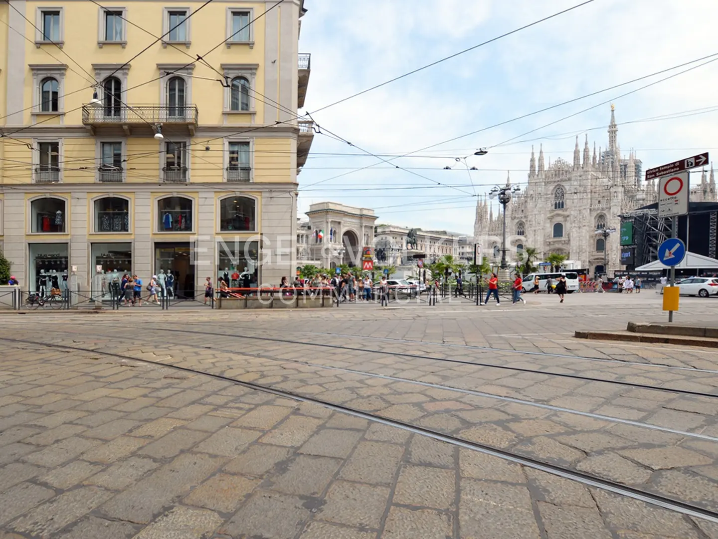 Street view of Milan, Italy, with the Duomo cathedral in the background. A yellow building with a store is on the left.