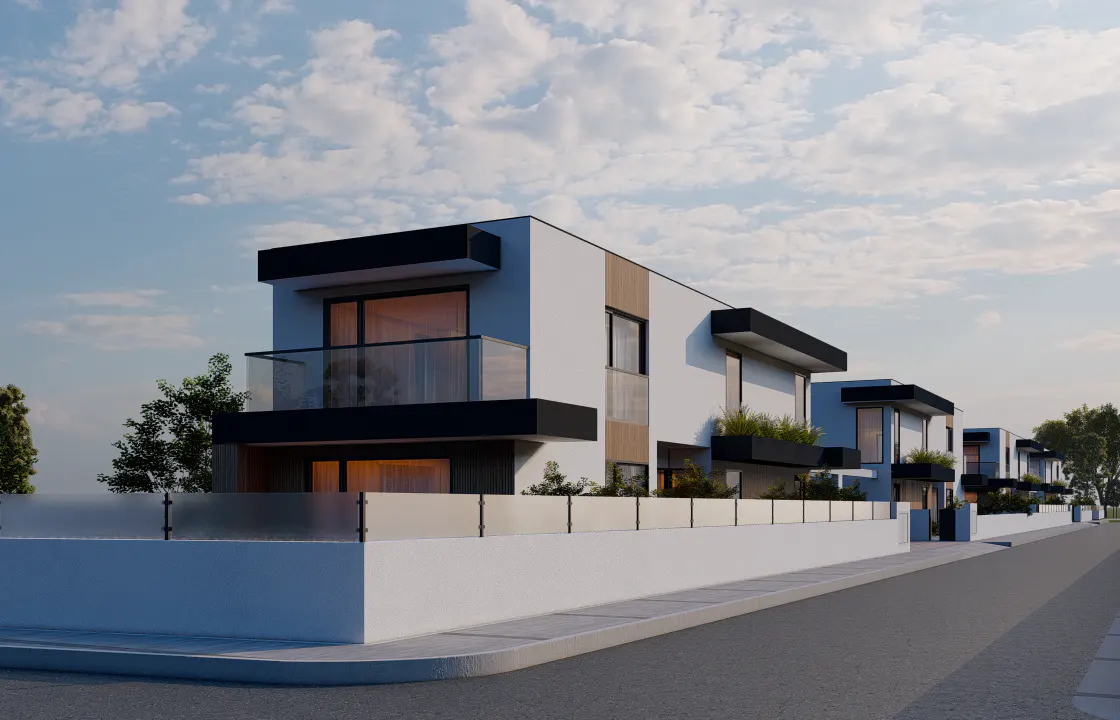 Modern townhouses with white walls, black trim, and glass balconies line a street under a cloudy sky.