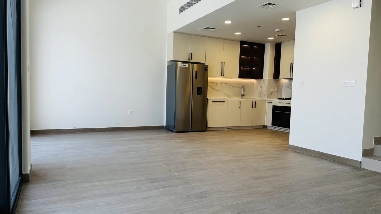 An open-concept apartment with a stainless steel refrigerator, white cabinets, and light gray wood-look tile flooring.
