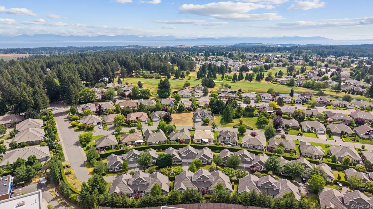 Aerial view of a suburban neighborhood with many houses, lush green trees, and distant mountains under a blue sky.