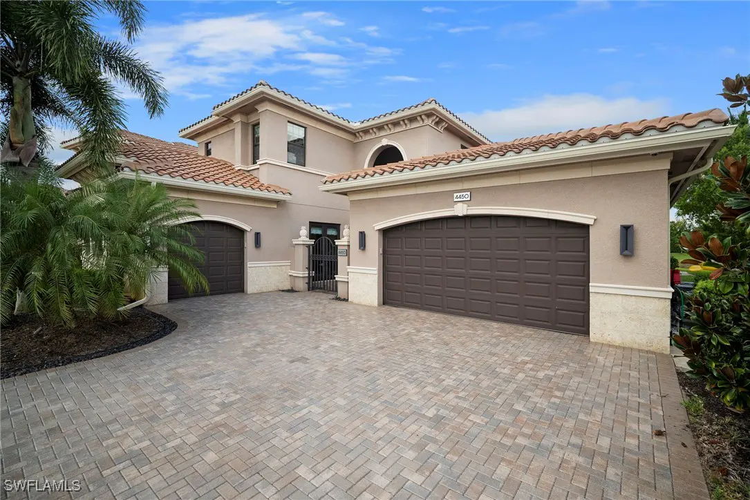 Beige two-story house with brown garage doors, a red tile roof, and a brick driveway.