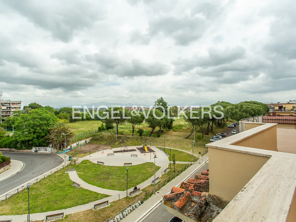 View from a building overlooking a park with green grass, trees, benches, and a playground under a cloudy sky.