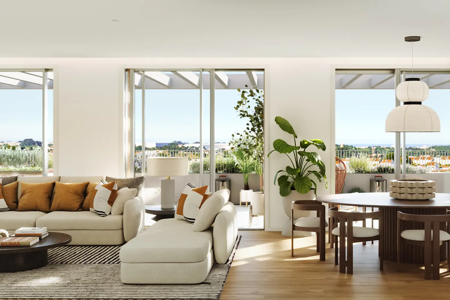 Modern living room with cream sofa, round dining table, large windows, and a balcony with plants and a scenic view.