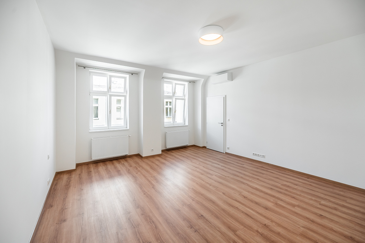Bright, empty room with wood floors, white walls, two windows, a door, and a ceiling light.