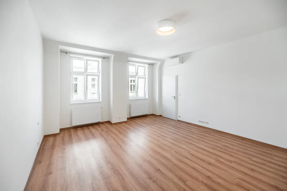 Bright, empty room with wood floors, white walls, two windows, a door, and a ceiling light.