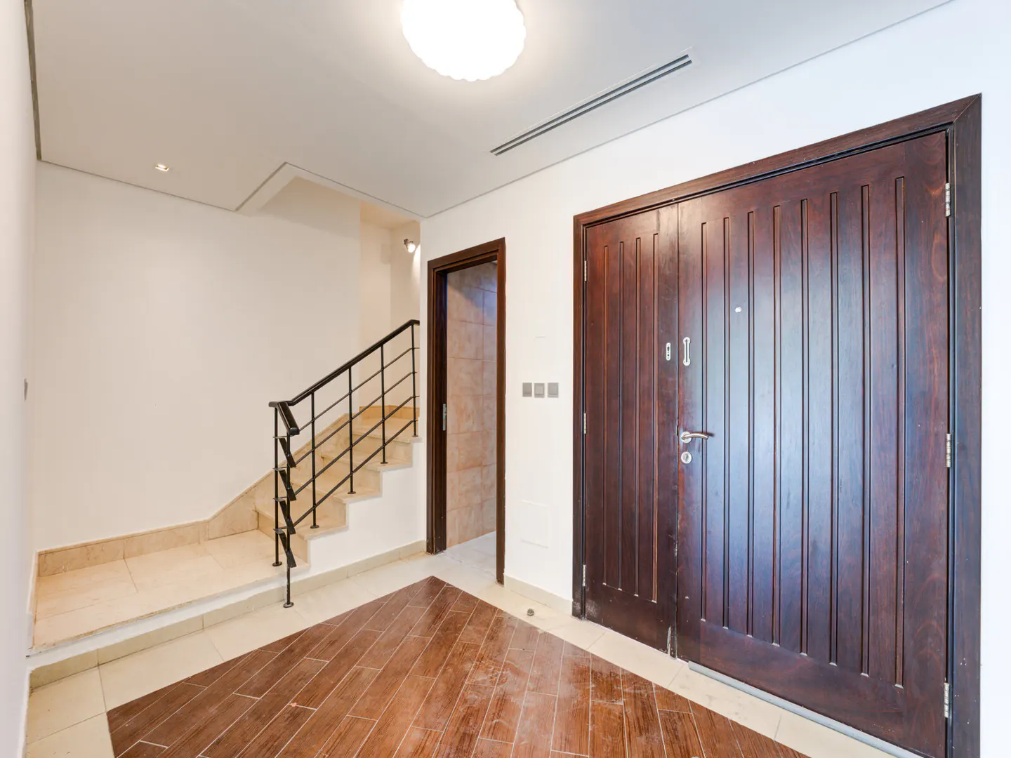 A bright foyer with a dark wood door, a staircase with black railings, and wood-look tile flooring.