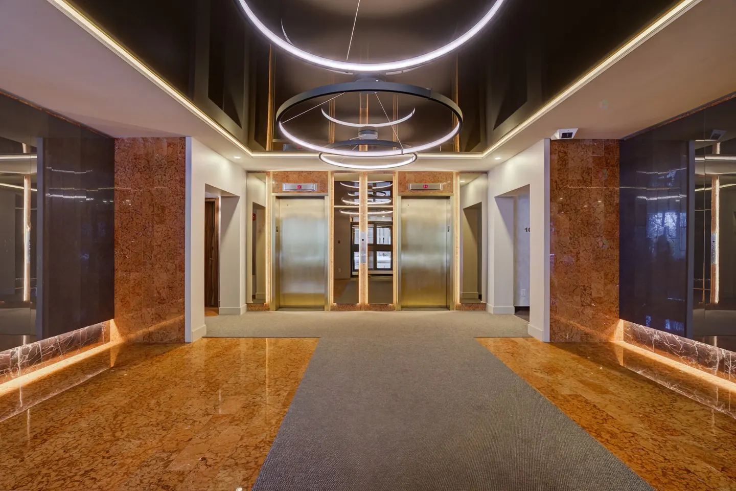 Modern lobby with three gold elevators, marble walls, and circular light fixtures.