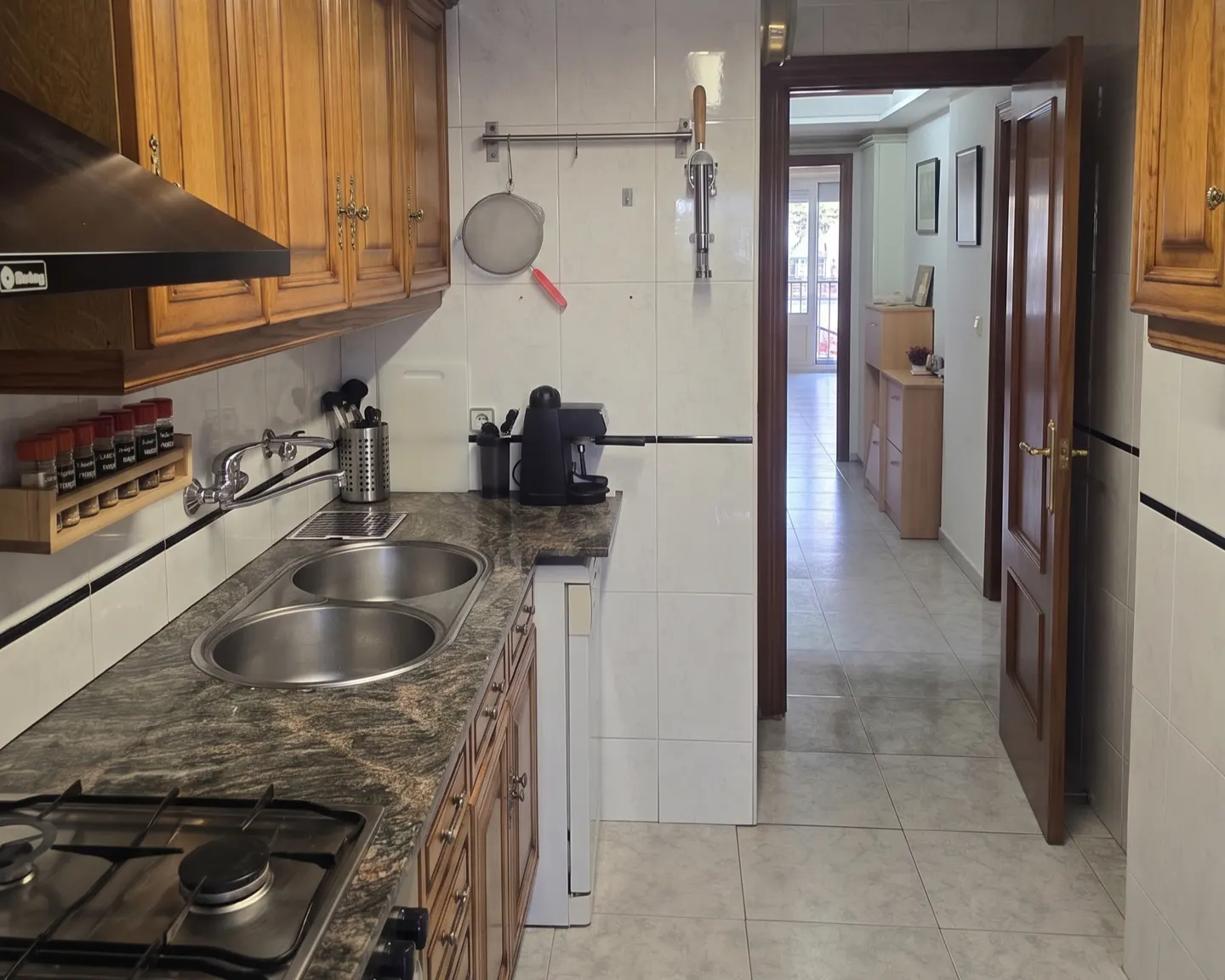 A kitchen with wood cabinets, a stainless steel sink, and a gas stove. A doorway leads to a hallway.