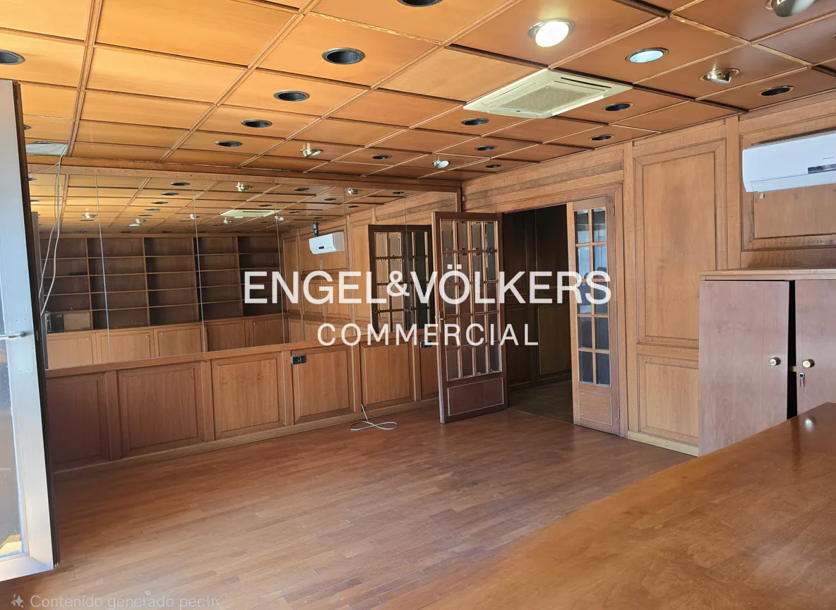 Office space with wood paneling, hardwood floors, and mirrored wall reflecting bookshelves. Doors lead to another room.