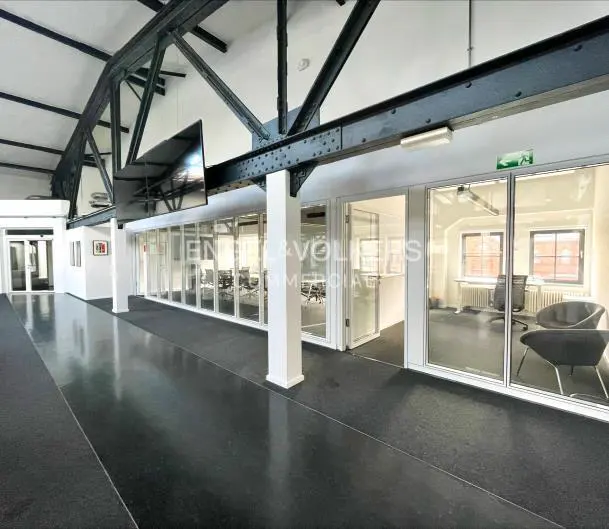 Modern office hallway with black floors, white walls, exposed black steel beams, and glass-walled meeting rooms.