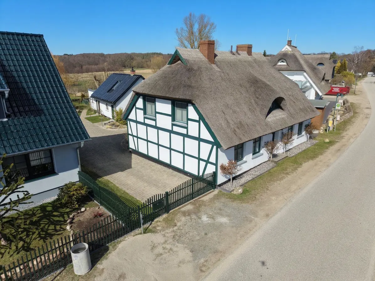 A white half-timbered house with a thatched roof on a sunny day.