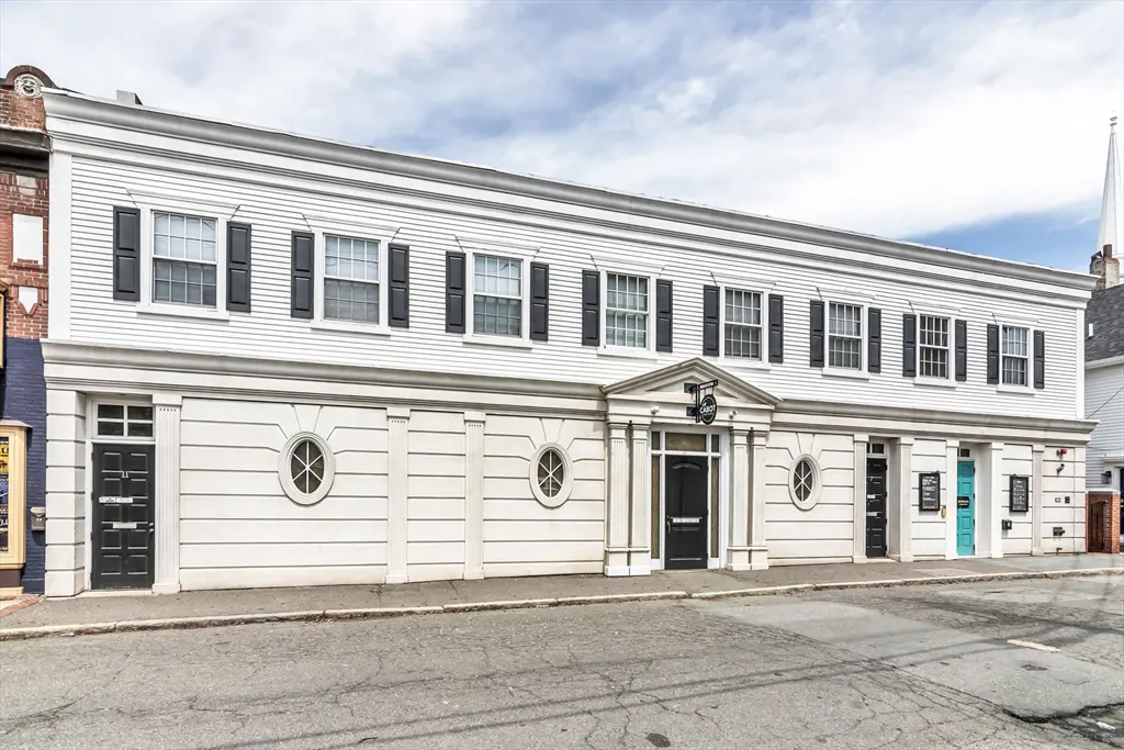 Two-story white building with black shutters and doors, and round windows on the first floor.