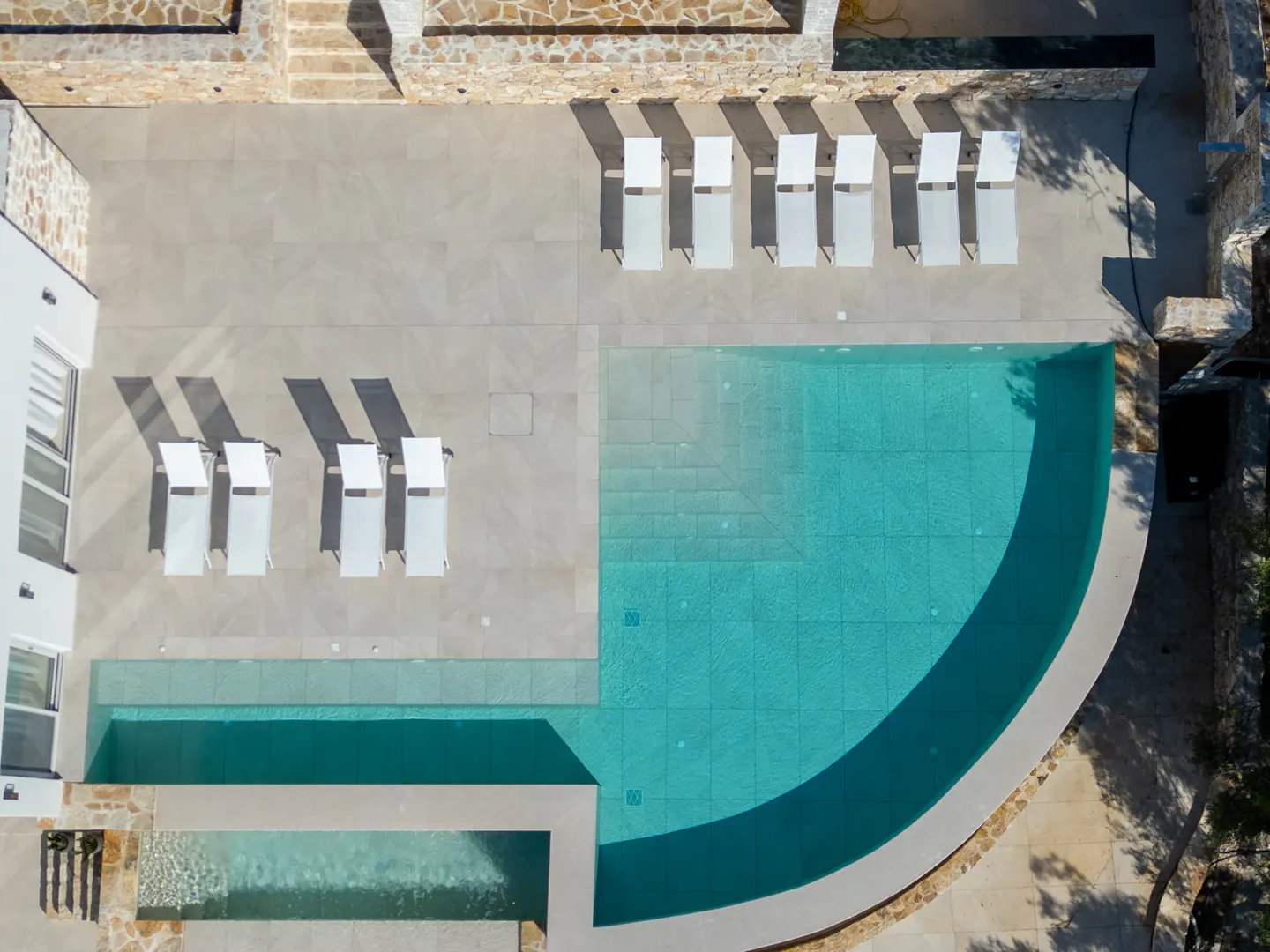 Aerial view of a luxury villa with a turquoise pool and white lounge chairs on a stone patio.