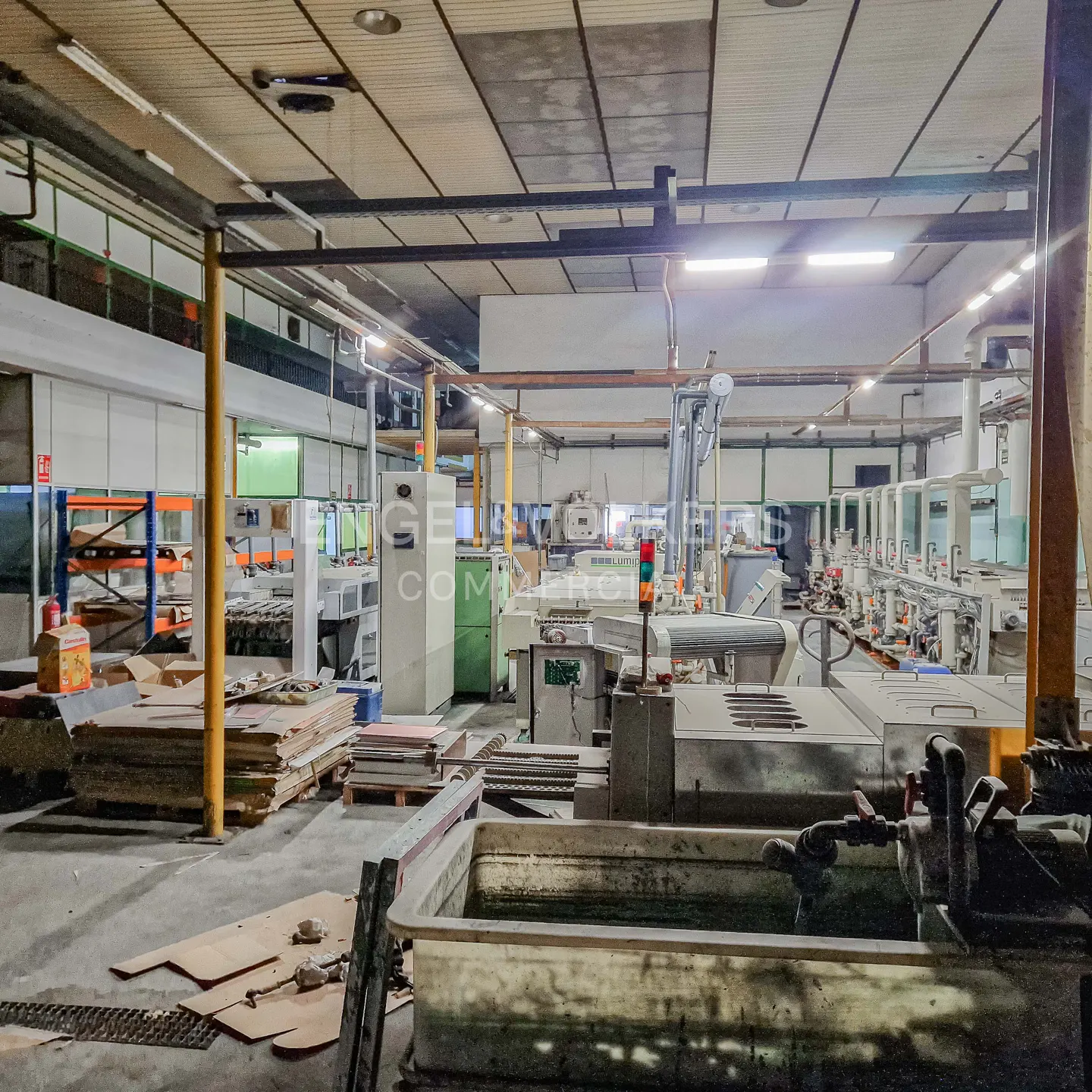 A wide shot of a large, empty industrial building with machinery and cardboard boxes.