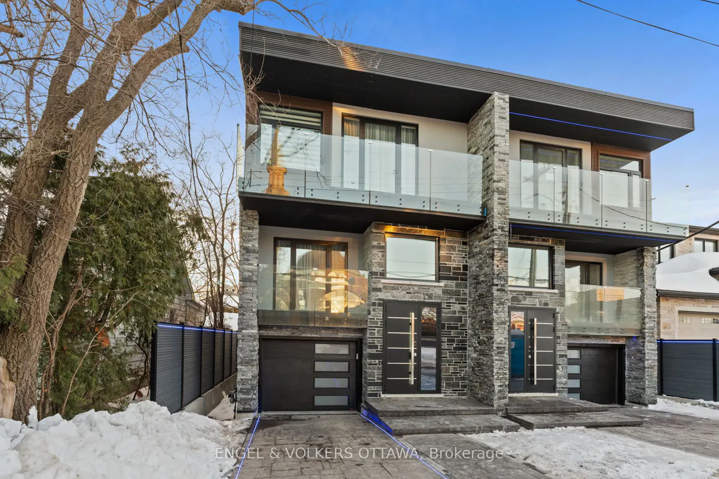 Exterior view of a modern two-story townhouse with stone accents, glass balconies, and black trim on a snowy day.