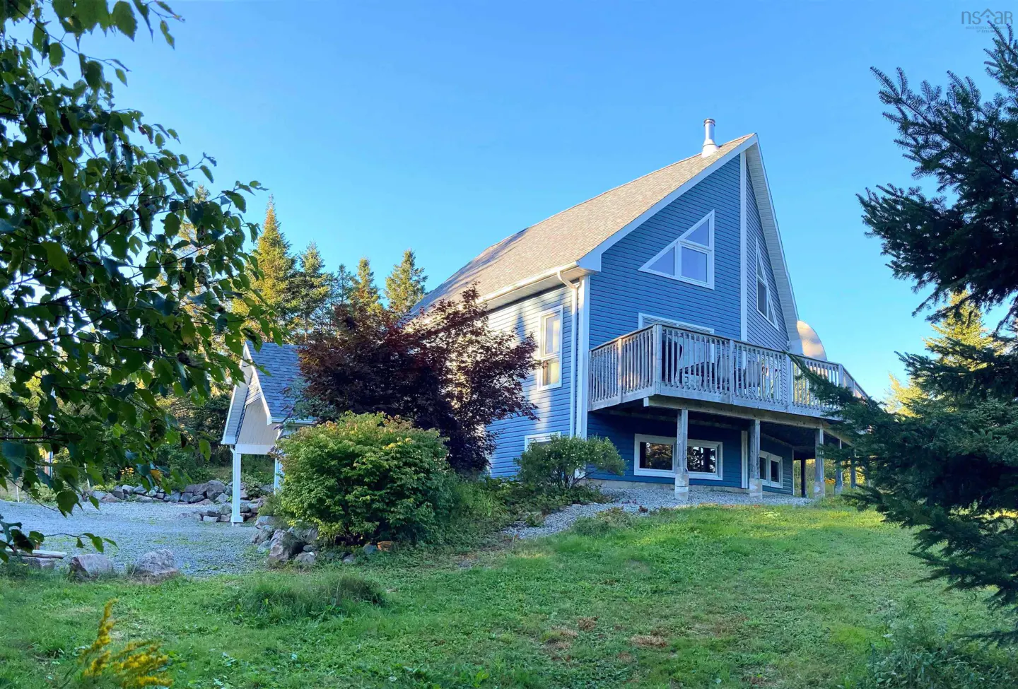 Blue two-story house with a deck, gray roof, and triangle window, surrounded by green trees and grass.