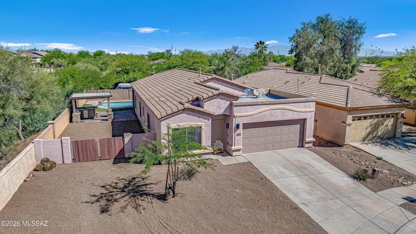 Aerial view of a single-story, stucco house with a brown tile roof, a two-car garage, and a fenced backyard with a pool.