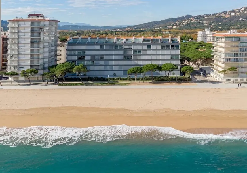 Oceanfront property featuring modern apartments with beach access. Turquoise water meets sandy shore near buildings.