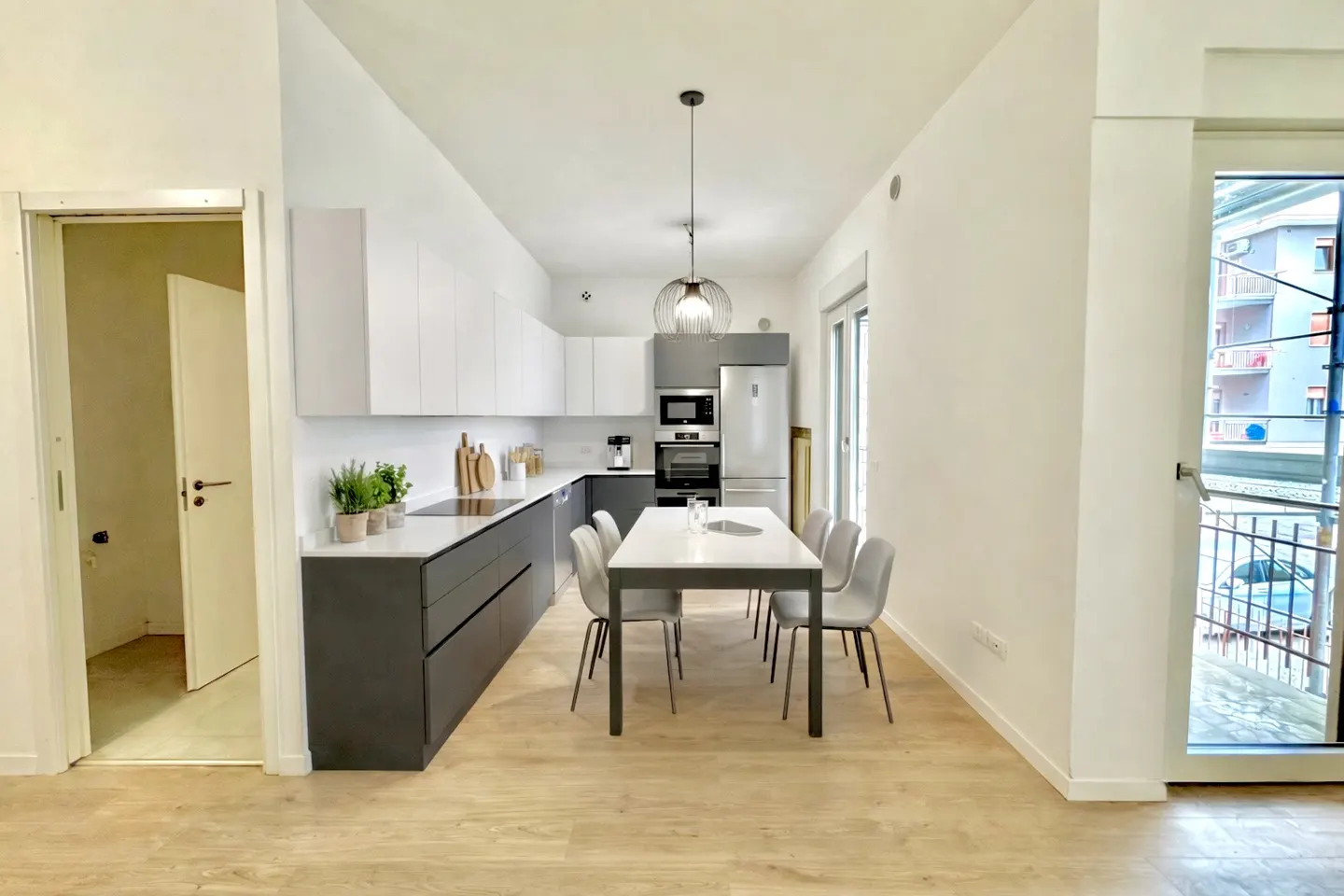 A modern kitchen with white cabinets, gray lower cabinets, and a white dining table with gray chairs. A door leads to another room.