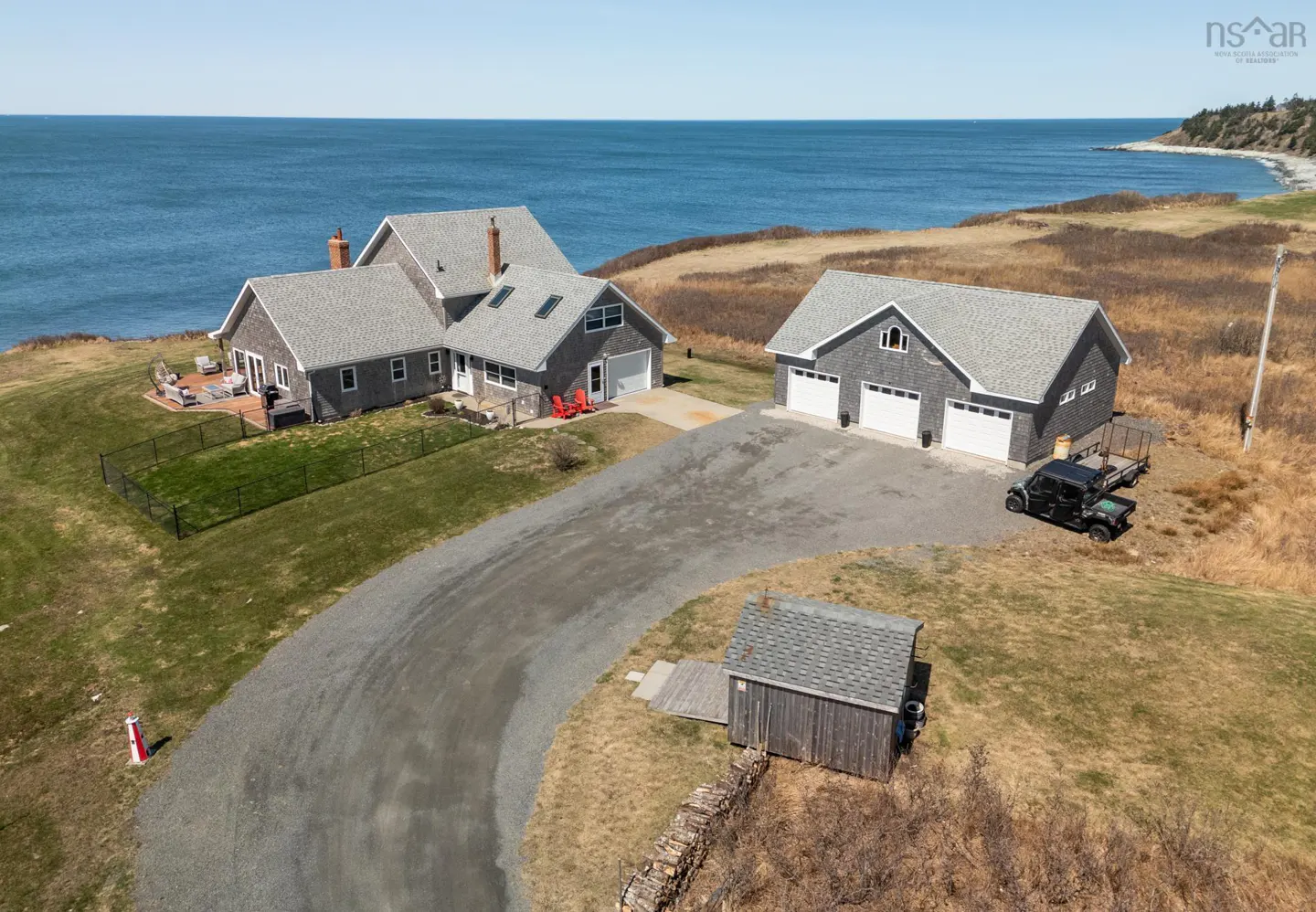 Aerial view of a gray shingled house and garage with a long driveway leading to the ocean.