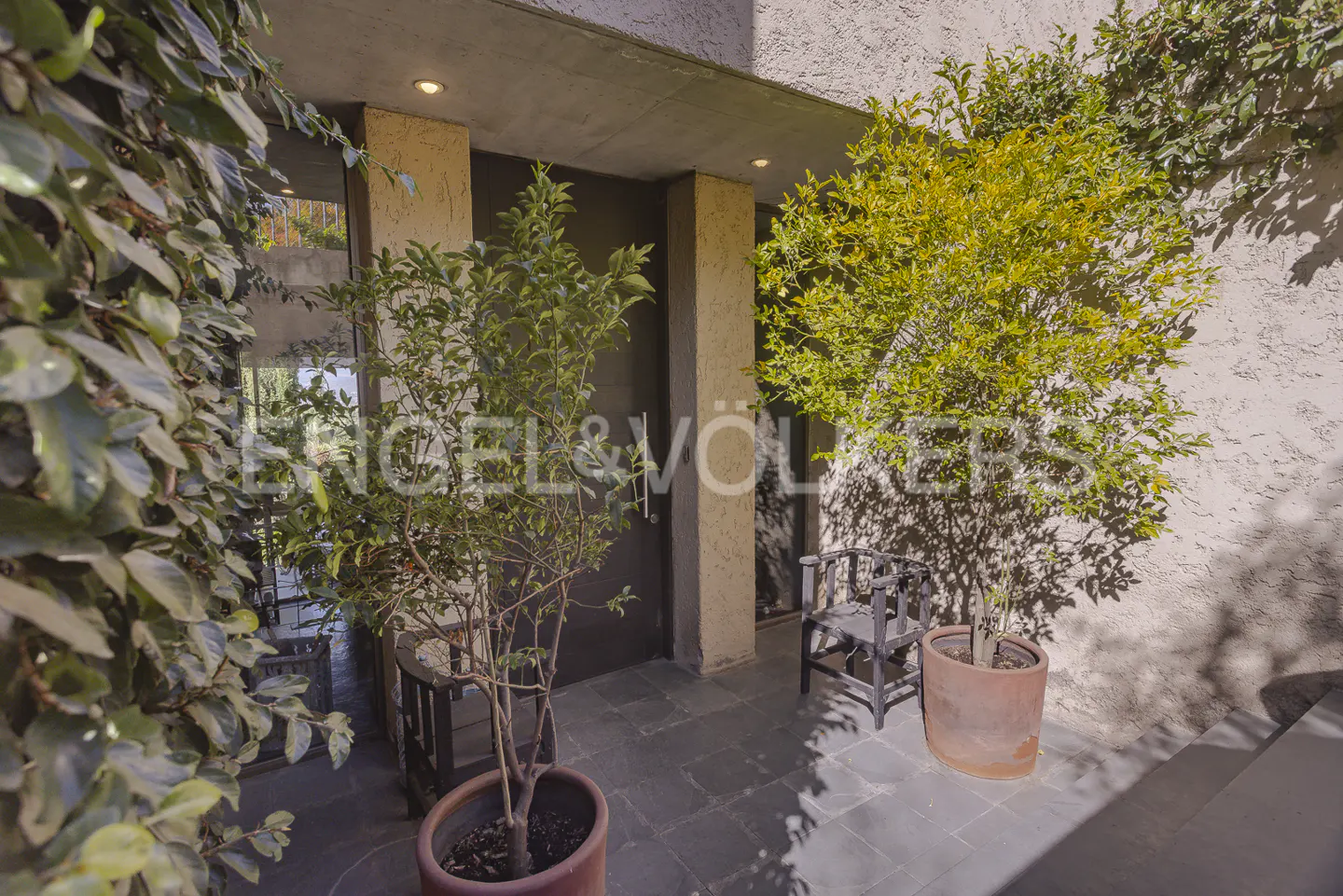 Exterior view of a home entrance with plants, a chair, and the Engel & Völkers logo.